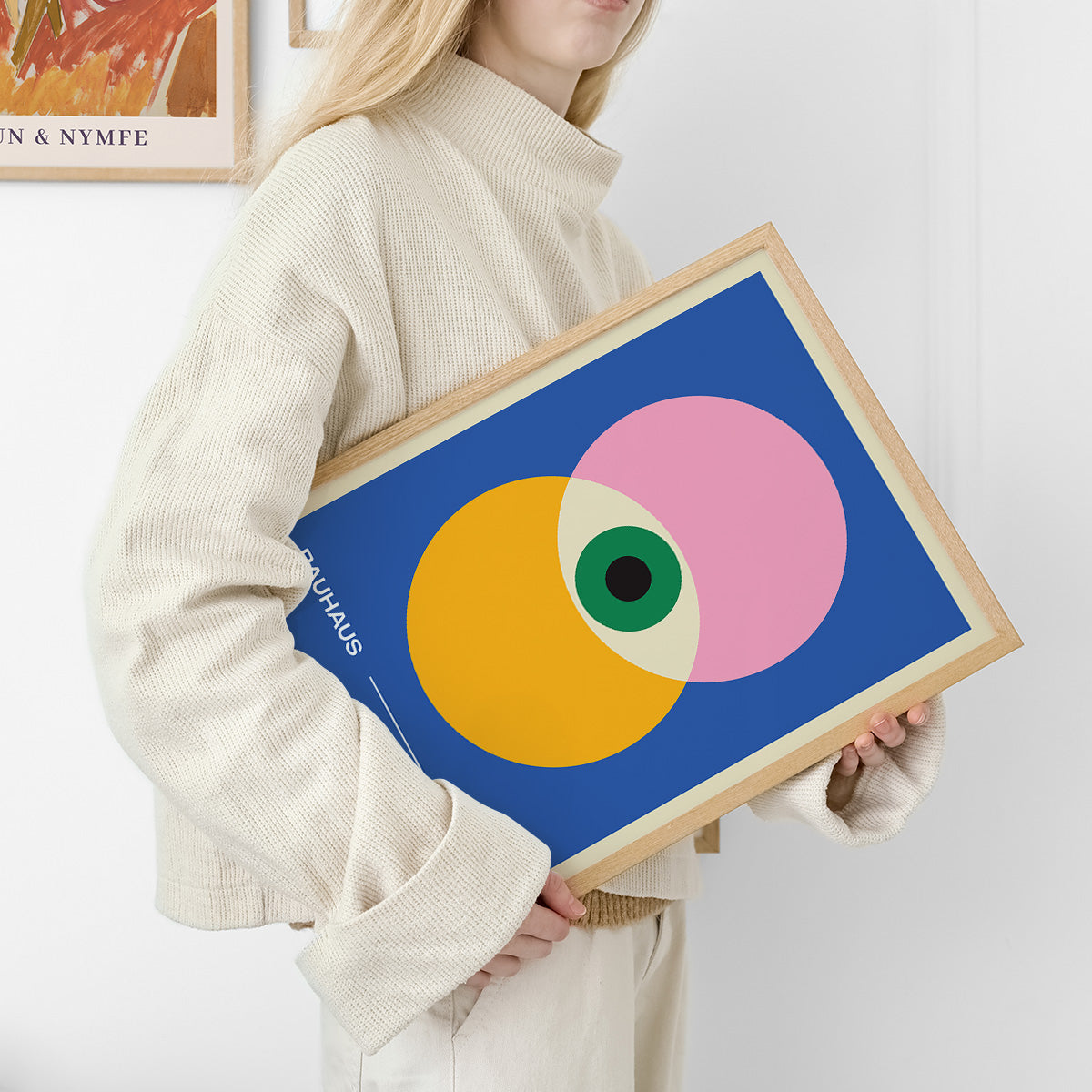 Kvinde holder en Bauhaus-plakat med geometriske former i gul, pink og blå.