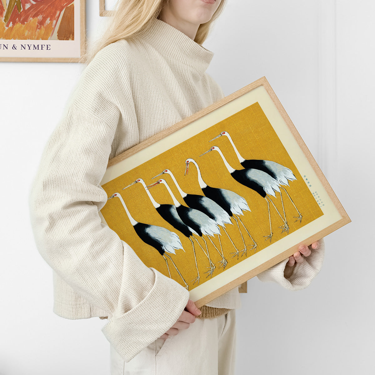 Kvinde i lys sweater holder en plakat med illustration af traner på gul baggrund.