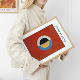 Hilma af Klint plakat med abstrakt design i røde, blå og gule farver, holdt af en person i lys tøj.