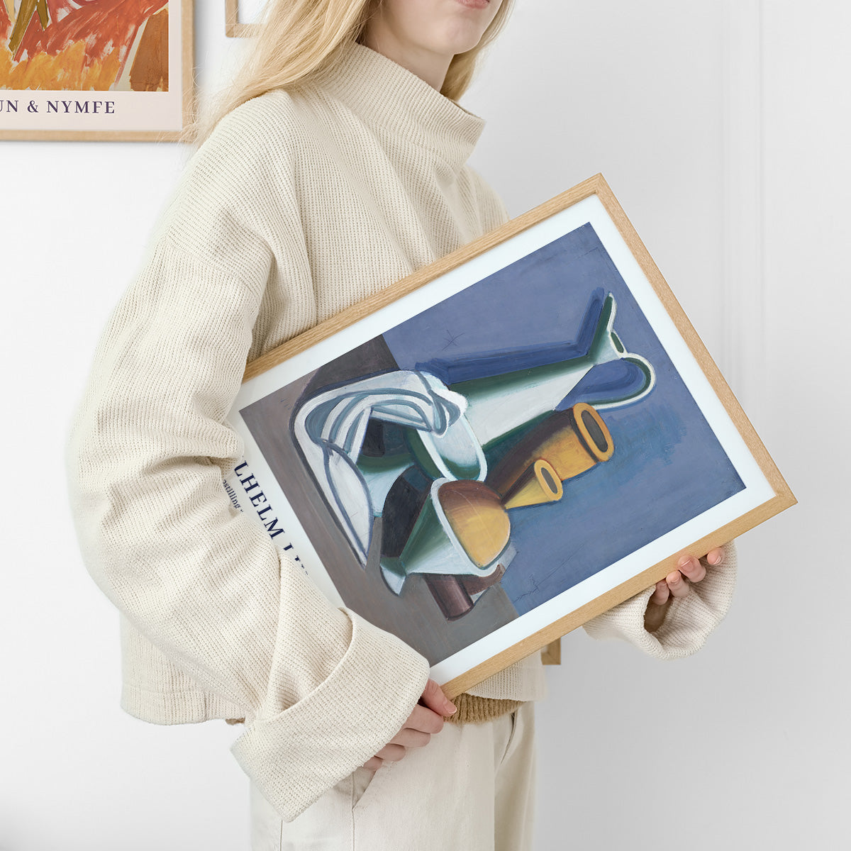 Kvinde i beige sweater holder en indrammet plakat med abstrakt kunstmotiv.