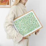 Kvinde holder en plakat med et grønt bladmønster i en træramme.