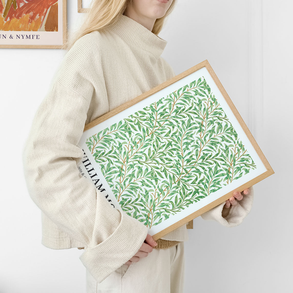 Kvinde holder en plakat med et grønt bladmønster i en træramme.