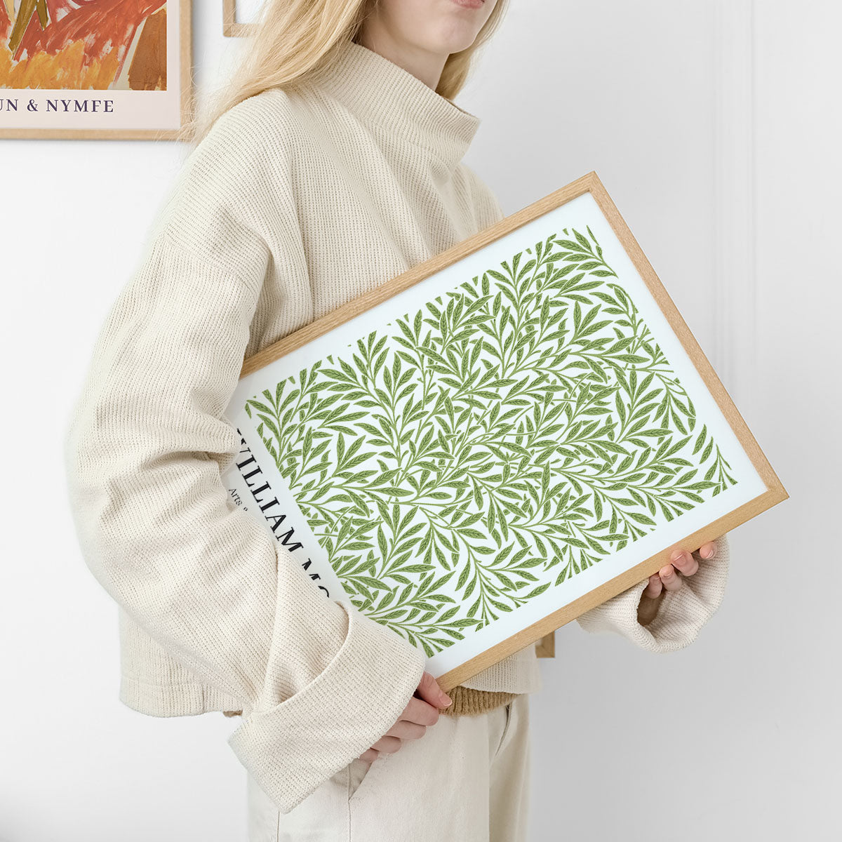 Plakat med grønt bladmønster af William Morris, holdt af en person i lyse, neutrale farver.
