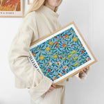 Kvinde holder en indrammet plakat med et blomstermønster i blå, grøn og rød, designet af William Morris.