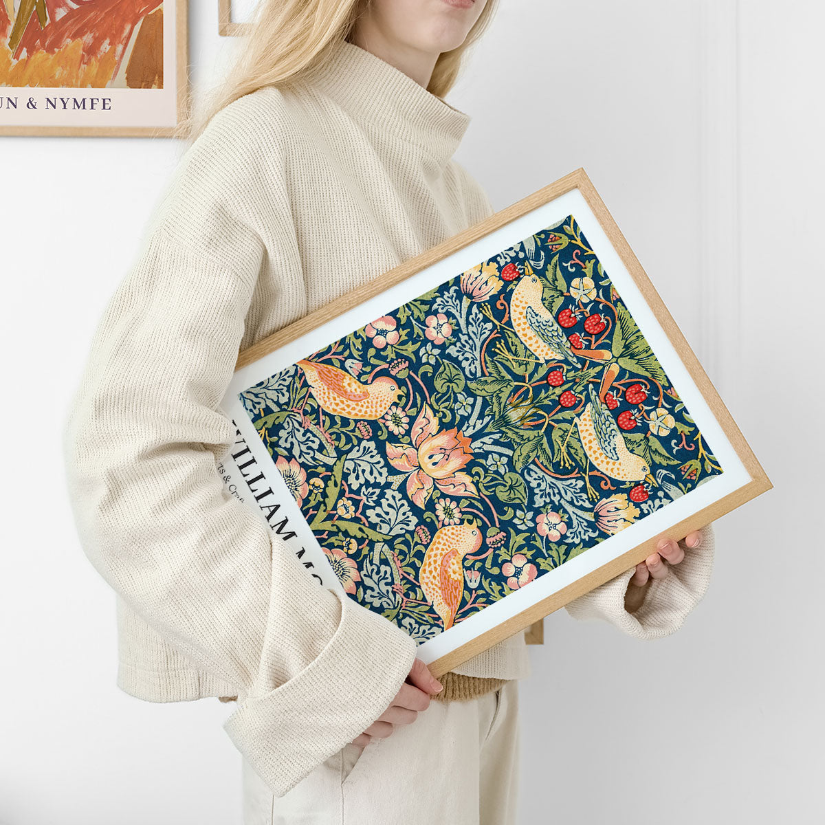 Kvinde holder en indrammet plakat med et farverigt, botanisk design af William Morris.