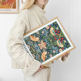 Kvinde holder en indrammet plakat med et farverigt, botanisk design af William Morris.
