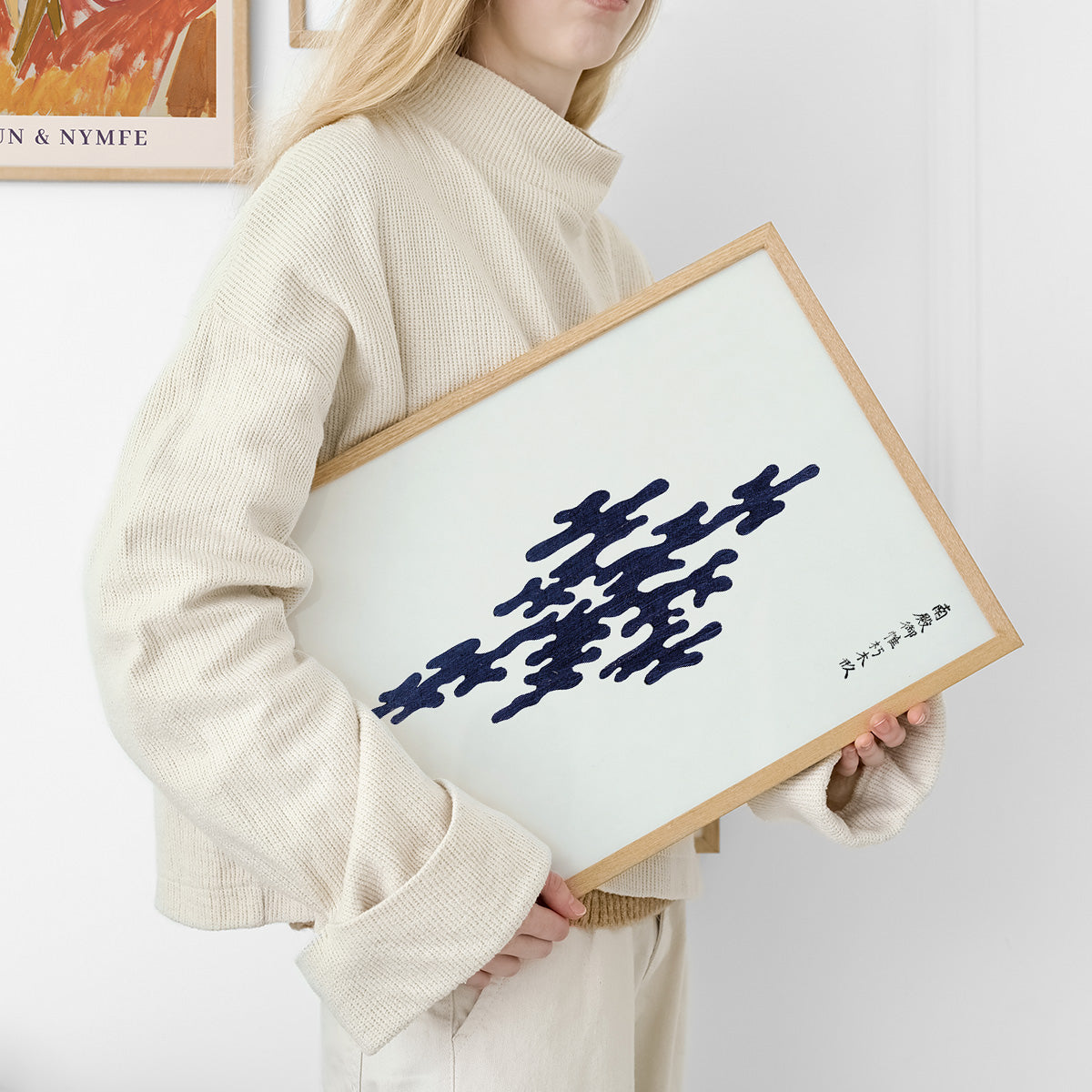 Plakat med abstrakt design i sort på hvid baggrund, indrammet i træ.
