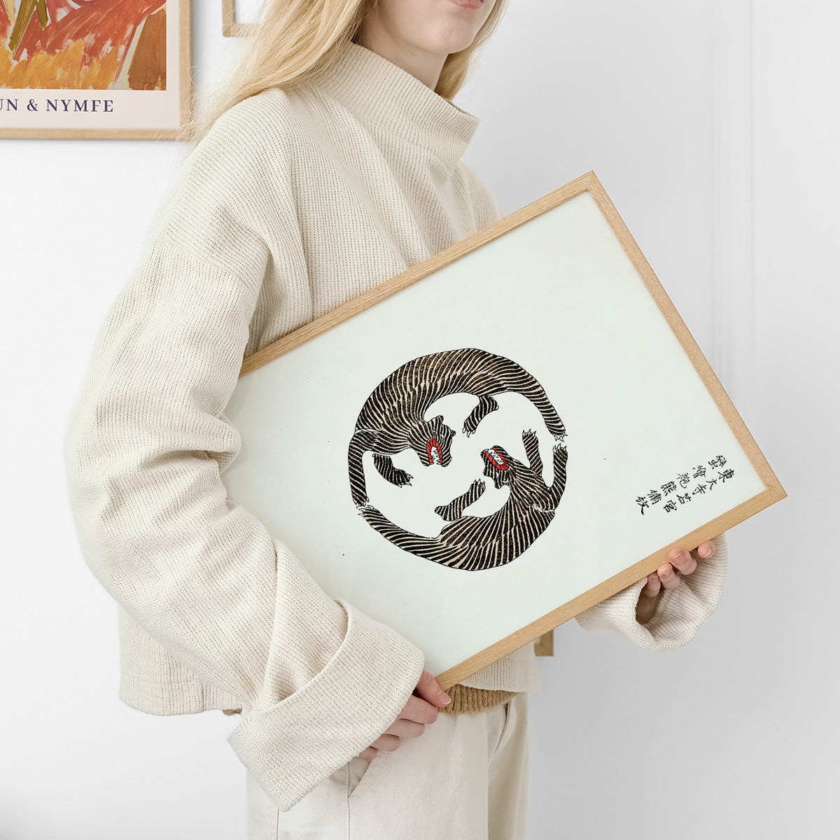 Kvinde i lys tøj holder en plakat med et tigerdesign i en træramme.