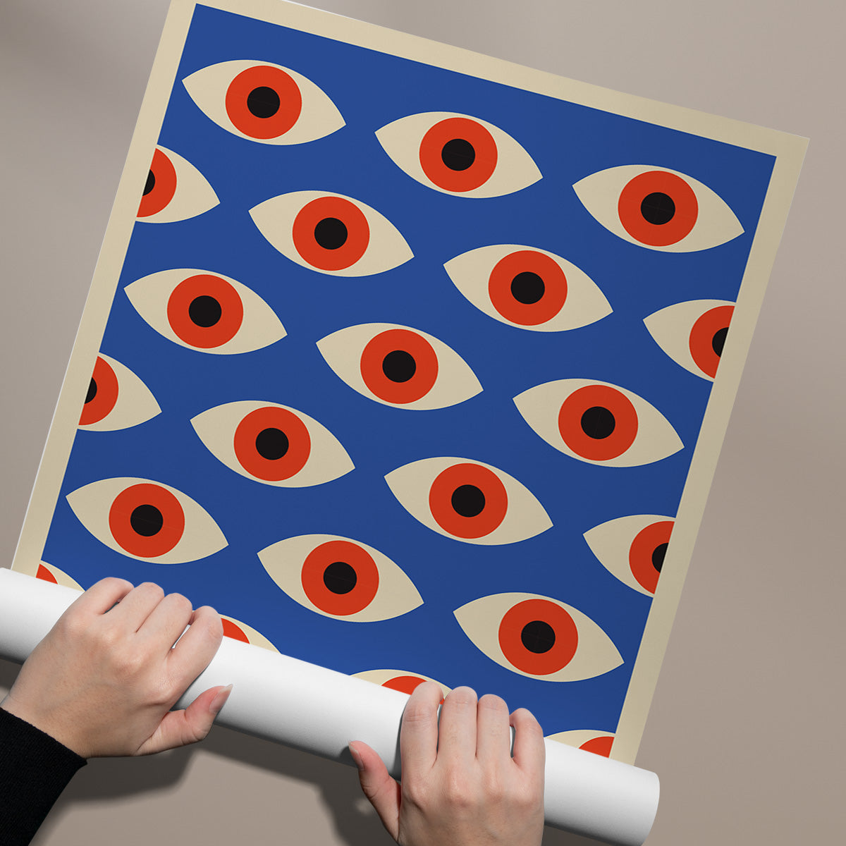 Plakat med et mønster af stiliserede øjne i røde og beige nuancer på en blå baggrund, holdt af to hænder.