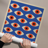 Plakat med et mønster af stiliserede øjne i røde og beige nuancer på en blå baggrund, holdt af to hænder.