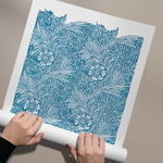 Plakat med blåt blomstermønster af William Morris, rullet ud på en beige baggrund.