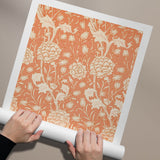 Plakat med et blomstermønster i beige og orange nuancer, der holdes af to hænder.