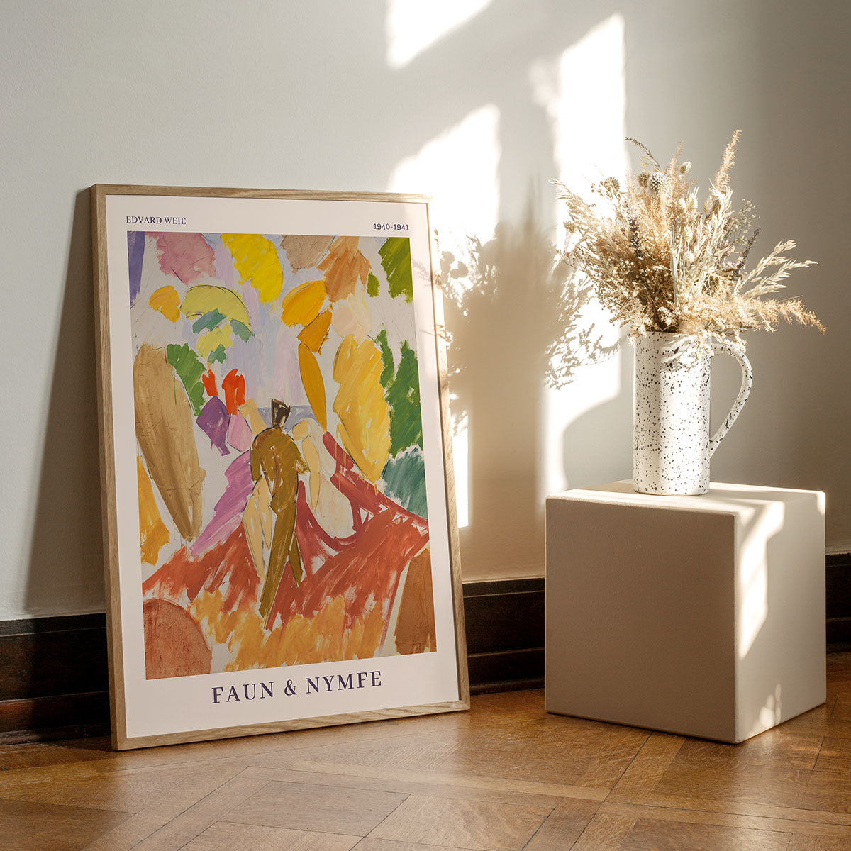 Faun & Nymfe kunstplakat af Edvard Weie, vist på et trægulv og lænet op ad en væg. Det farverige abstrakte maleri har livlige nuancer af gul, orange og grøn. En dekorativ vase med tørrede blomster står på en lille hvid piedestal i nærheden, oplyst af naturligt lys.