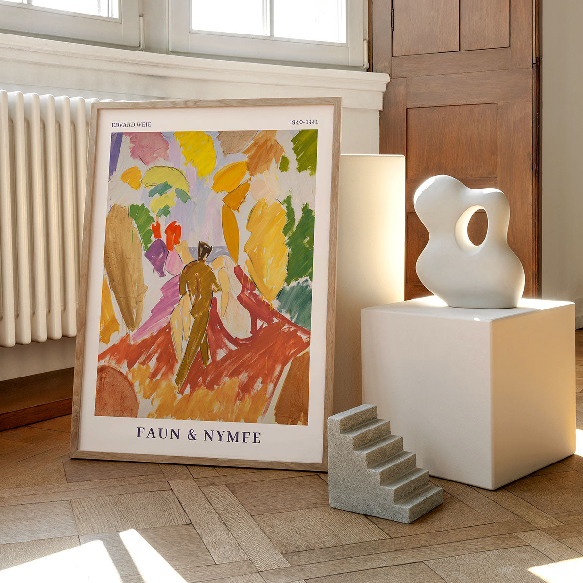 Farverig abstrakt kunstplakat med titlen Faun & Nymfe af Edvard Weie, vist på et trægulv ved siden af moderne skulpturer og en radiator, mens naturligt lys strømmer ind gennem et vindue.