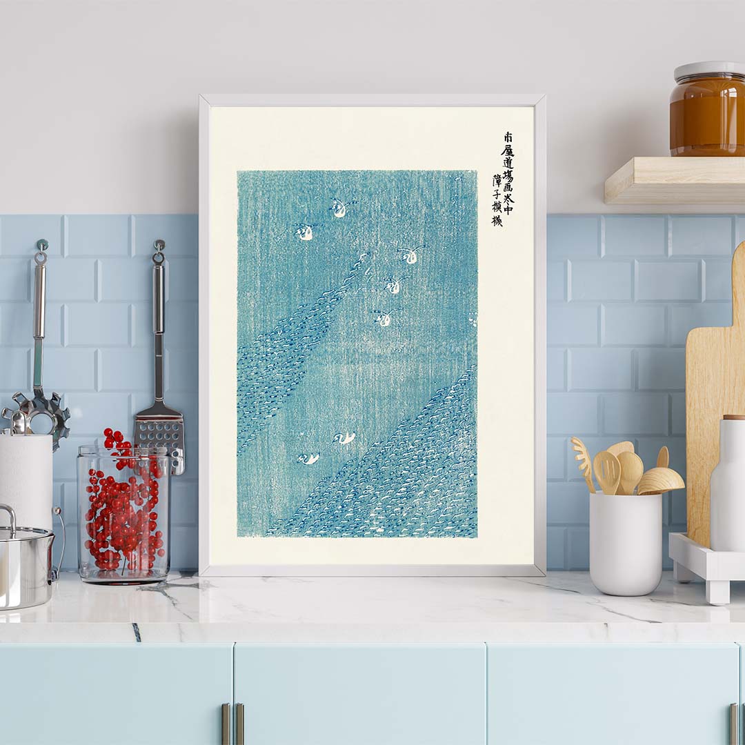 Plakat med blå og hvidt design af svaner på vandet, placeret i en moderne køkkenindretning.