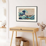 Plakat af "The Great Wave" af Katsushika Hokusai hængende på en væg over et træbord i et stilfuldt rum.