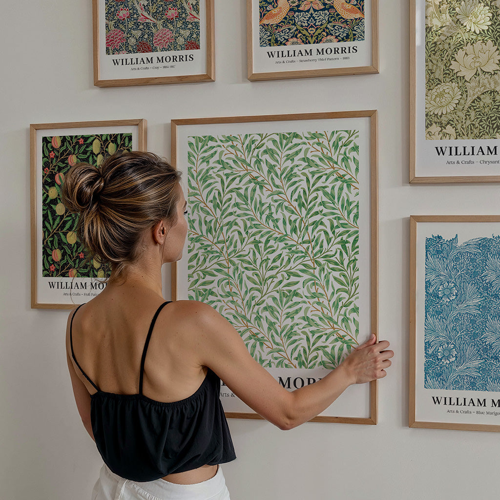 Kvinde hænger William Morris plakat op på plakatvæg ved siden af andre William Morris plakater