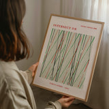 En person holder en indrammet Shima Shima Intersect plakat af Furuya Korin i hænderne.