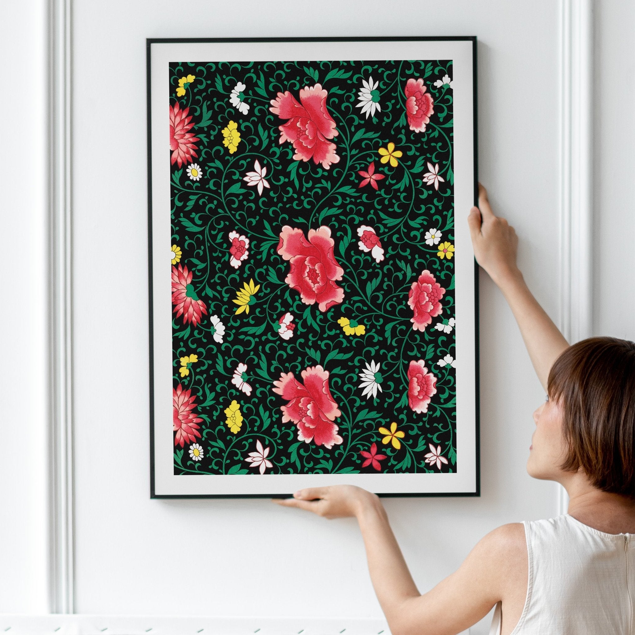 Plakat med hvide, gule og røde blomster i sort ramme på væg 